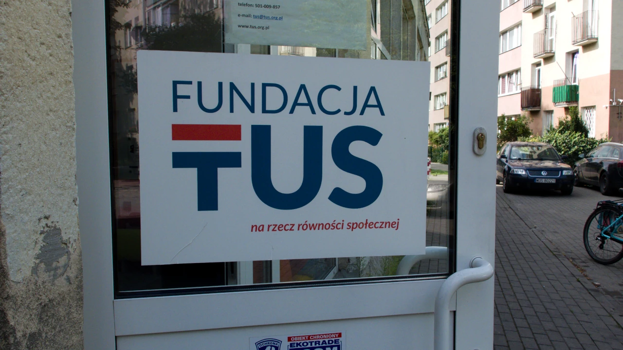 Otwarte drzwi do budynku. Na drzwiach naklejka z logo Fundacji TUS i napisem: na rzecz równości społecznej.