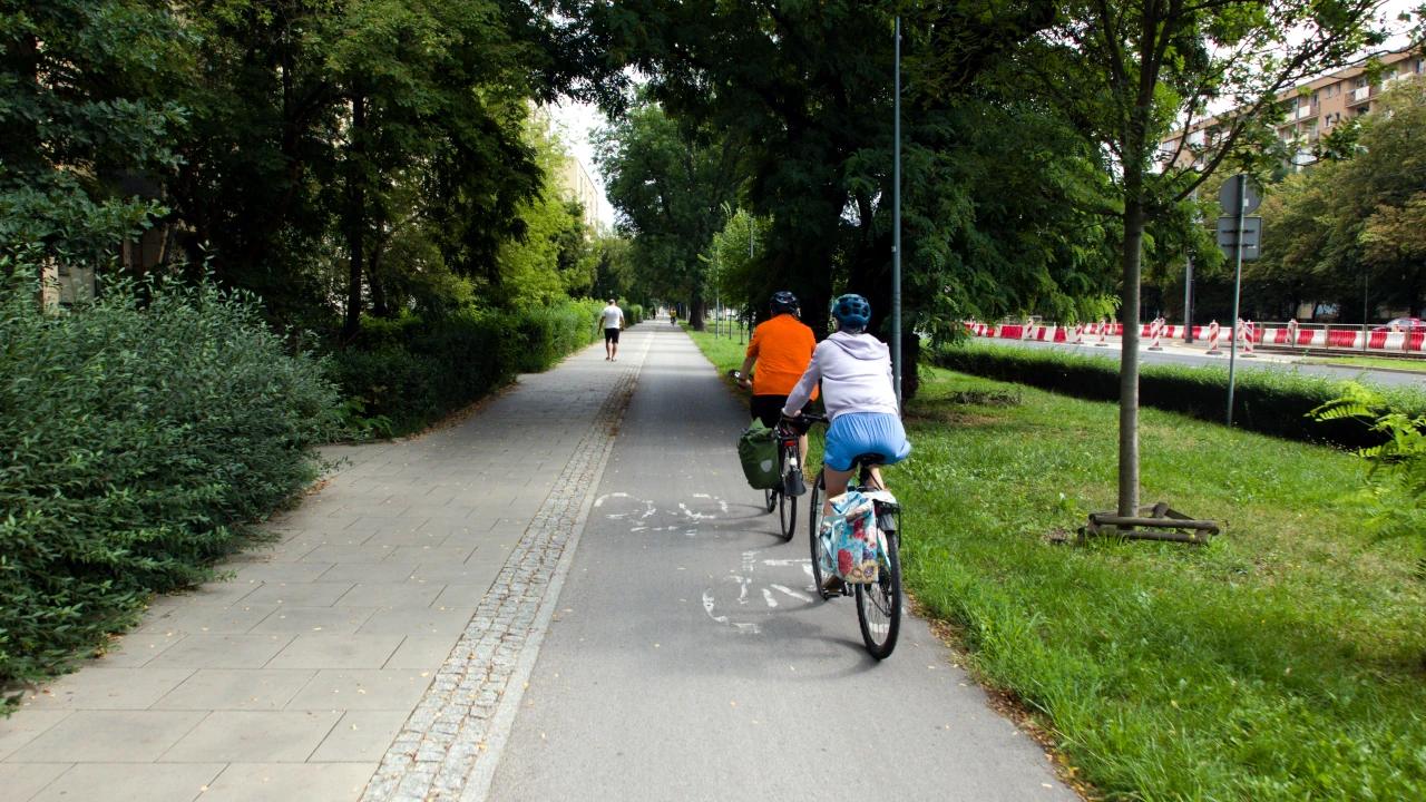 Dwoje zrowerowanych osób porusza się po drodze dla rowerów. Obok po chodniku przemieszczają się piesi.