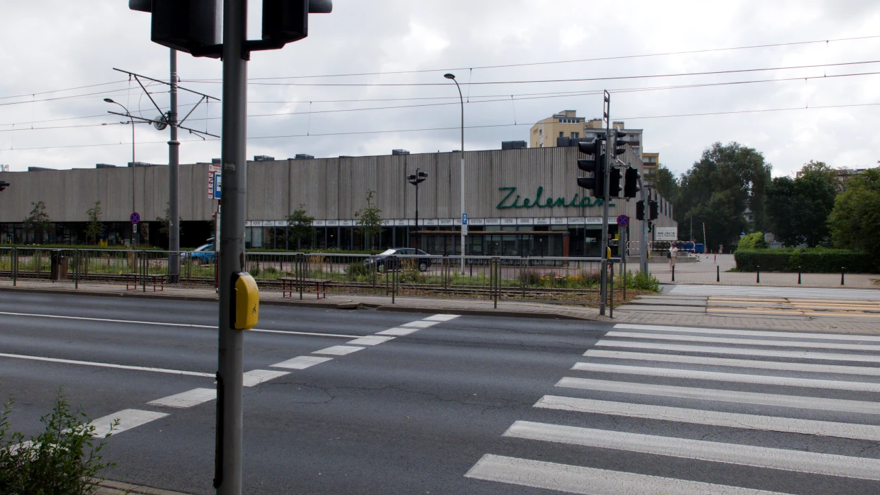 Przejście dla pieszych przez jezdnię i tory tramwajowe. W tle pawilon handlowy z napisem: Zieleniak.