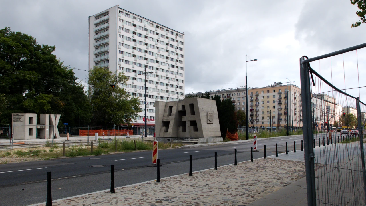 W tle jasny wieżowiec. Po lewej stronie ulicy część pomnika – betonowe liczby 8-IX i 1939.
