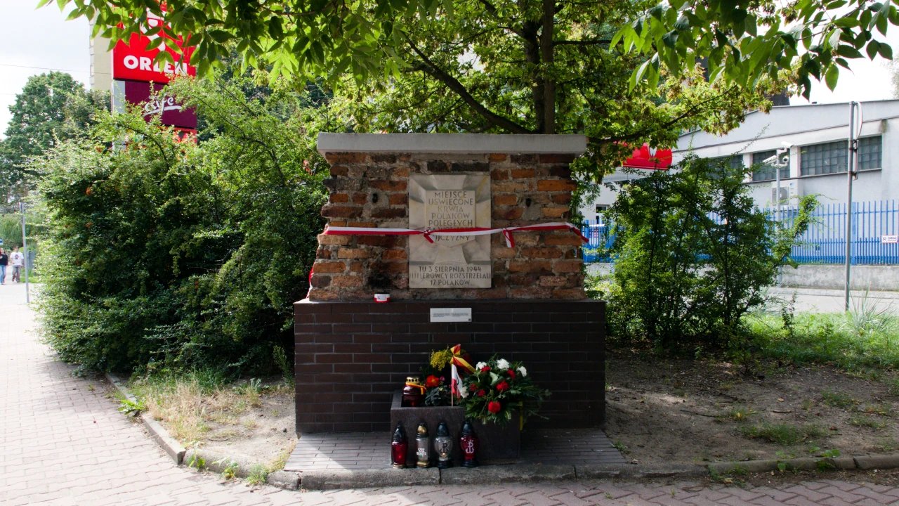 Fragment muru z tablicą poświęconą poległym Polakom. U podnóża kwiaty, wieńce, znicze.