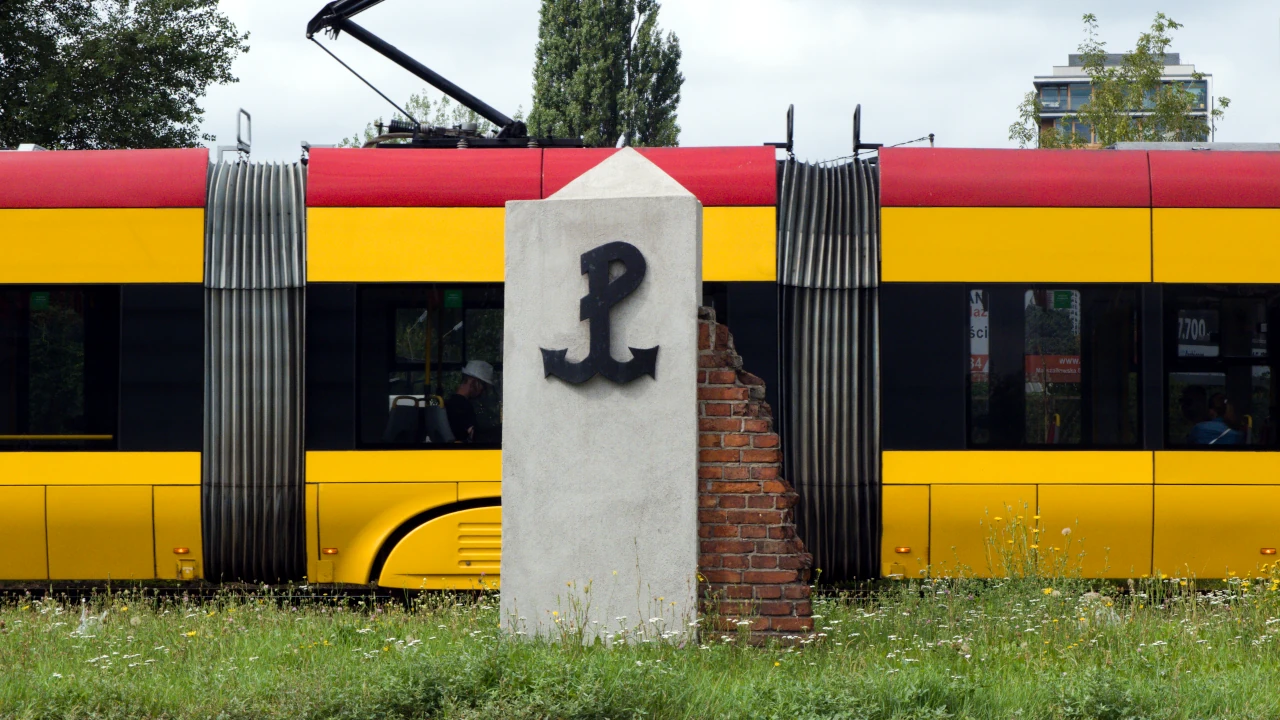 Mur z kotwicą Polski walczącej. W tle przejeżdżający tramwaj.