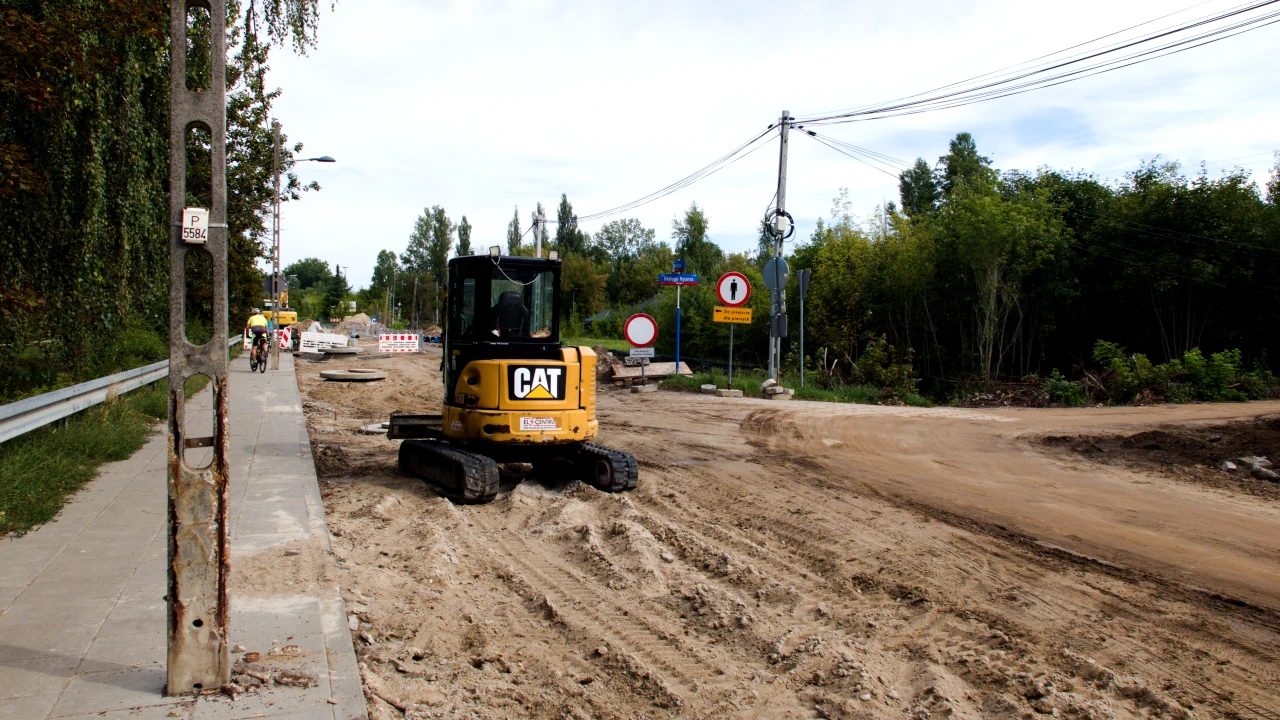 Roboty drogowe. Na pierwszym planie mała koparka, w tle rozkopana ulica.