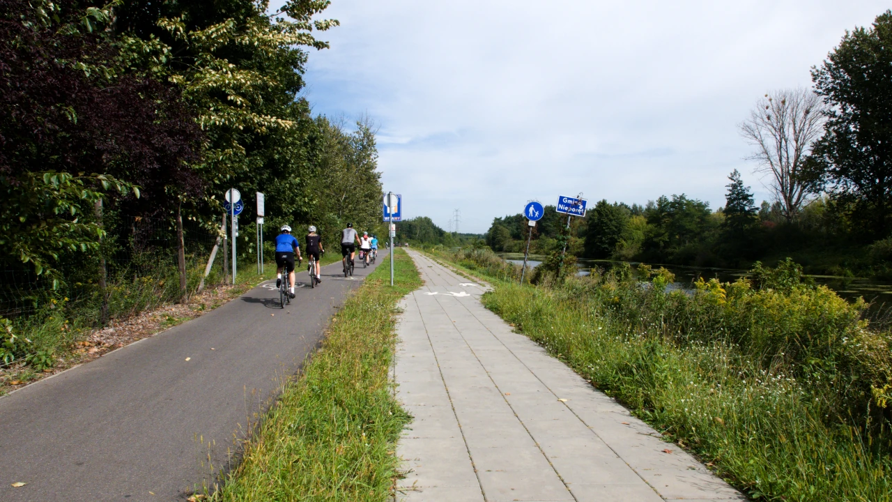 Droga dla rowerów z grupą kilku osób na rowerach. Po prawej stronie chodnik.